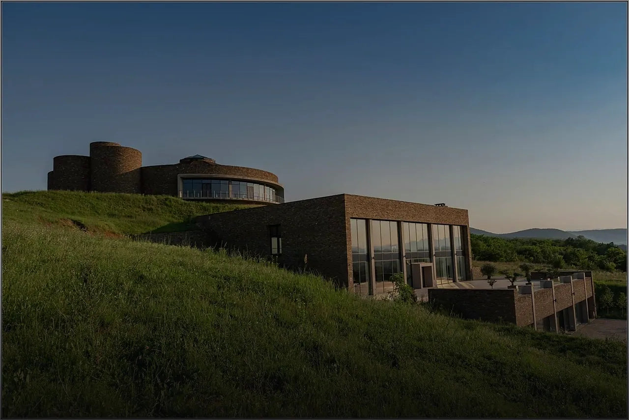 The stone and glass winery on its hillside at golden hour, its round tower rising above a long glazed hall.