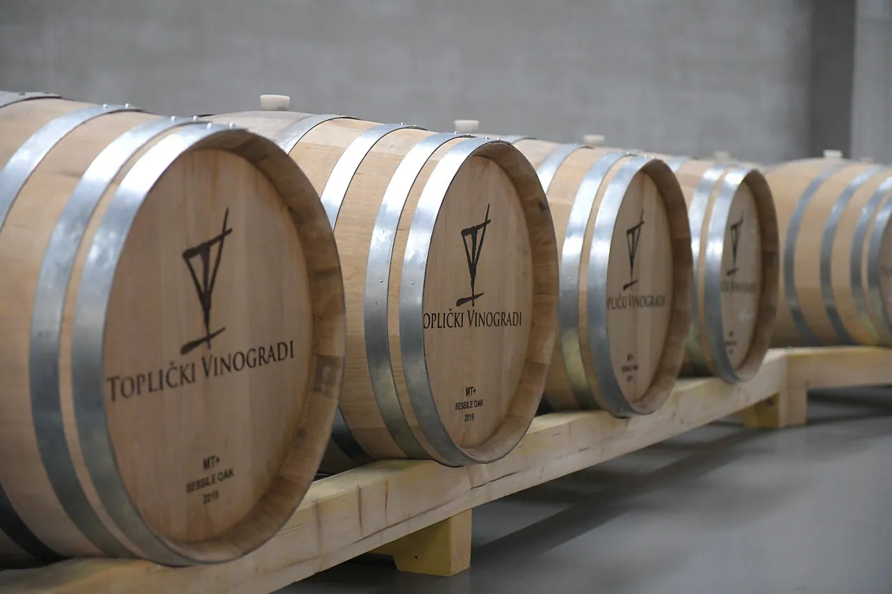 A row of new sessile oak barrels, each head branded with the estate mark and the words Toplički Vinogradi.