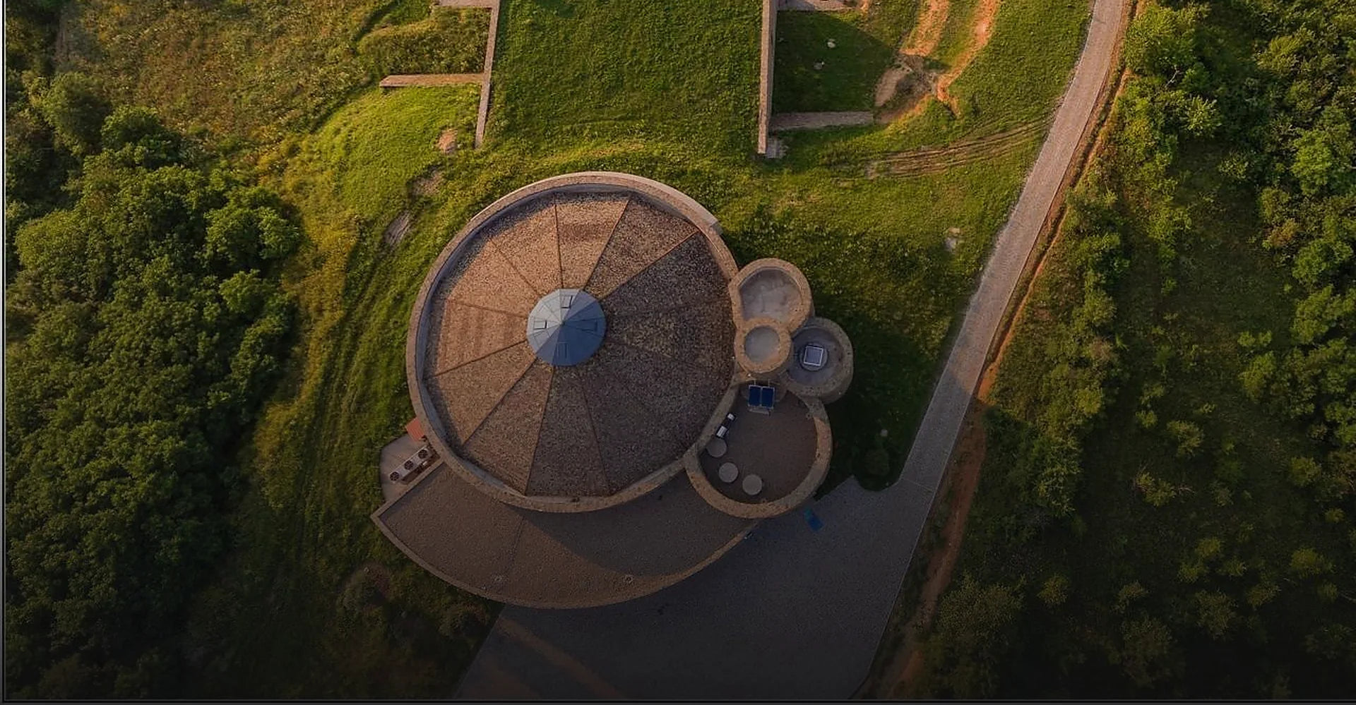 The round, spiral form of the Toplički Vinogradi winery seen from directly above, set into green hills.